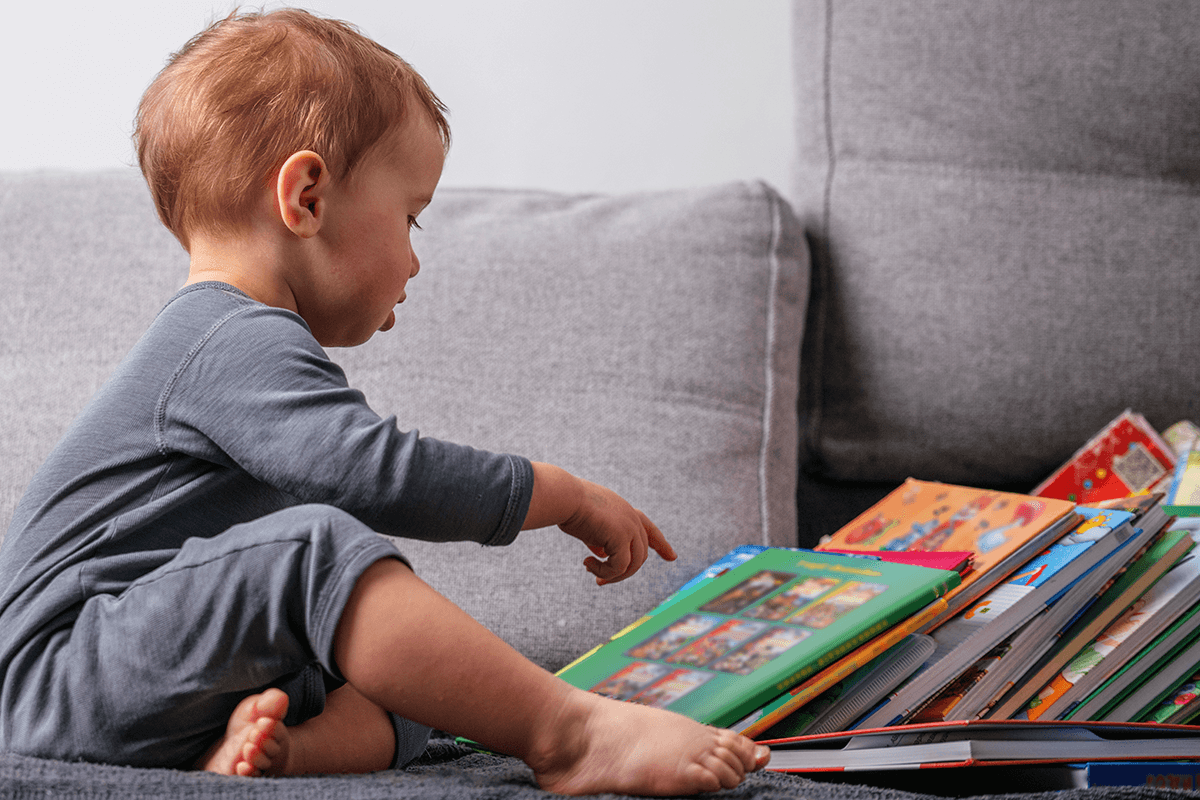 toddler pointing at a pile of books – recognizing the covers of books they love is a reading milestone for toddlers
